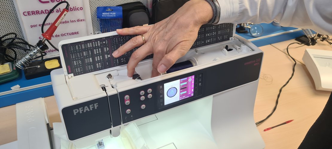 PFAFF creative 3.0 with the top cover open, a navy thread spool on the pin, Nuria threading the path.