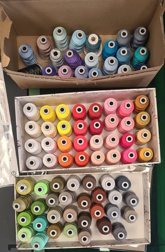 Three boxes holding dozens of embroidery thread spools sorted by colour.
