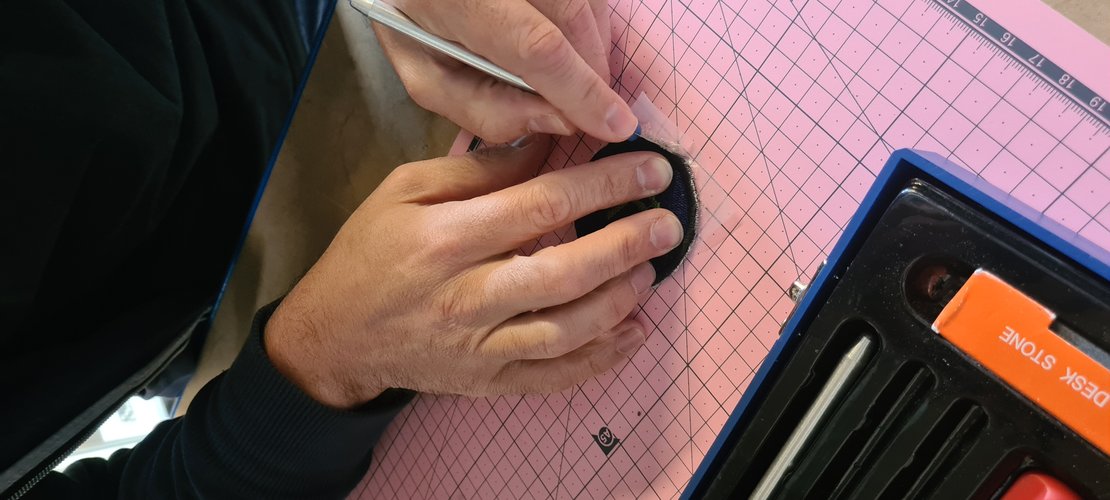 Trimming the patch to shape with a craft knife on a pink cutting mat.