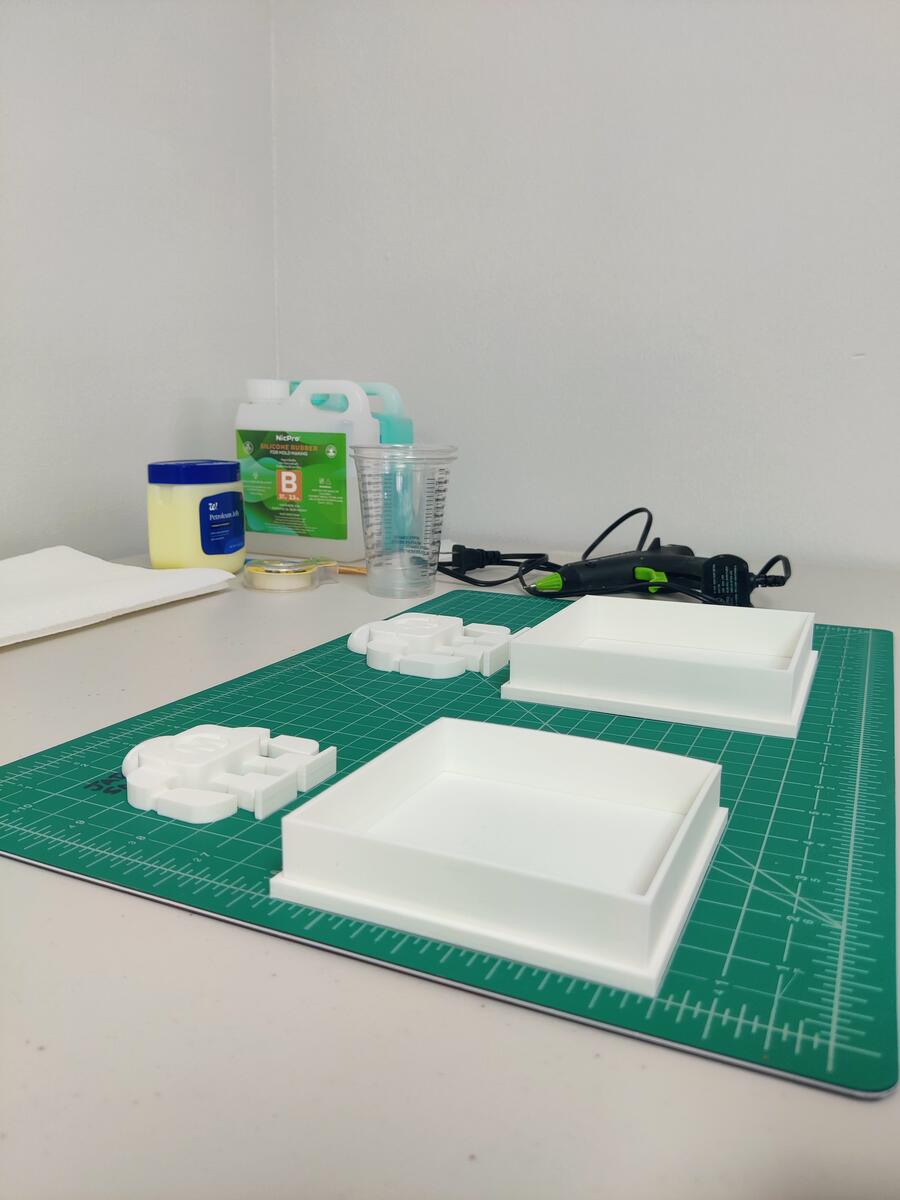 Mold boxes, silicone rubber Part B, petroleum jelly, and hot glue gun on cutting mat