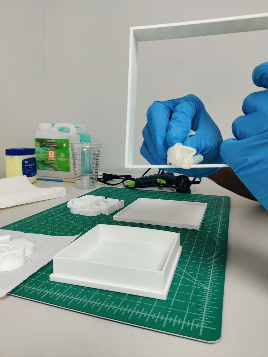 Blue gloved hands wiping down the mold box frame with isopropyl alcohol