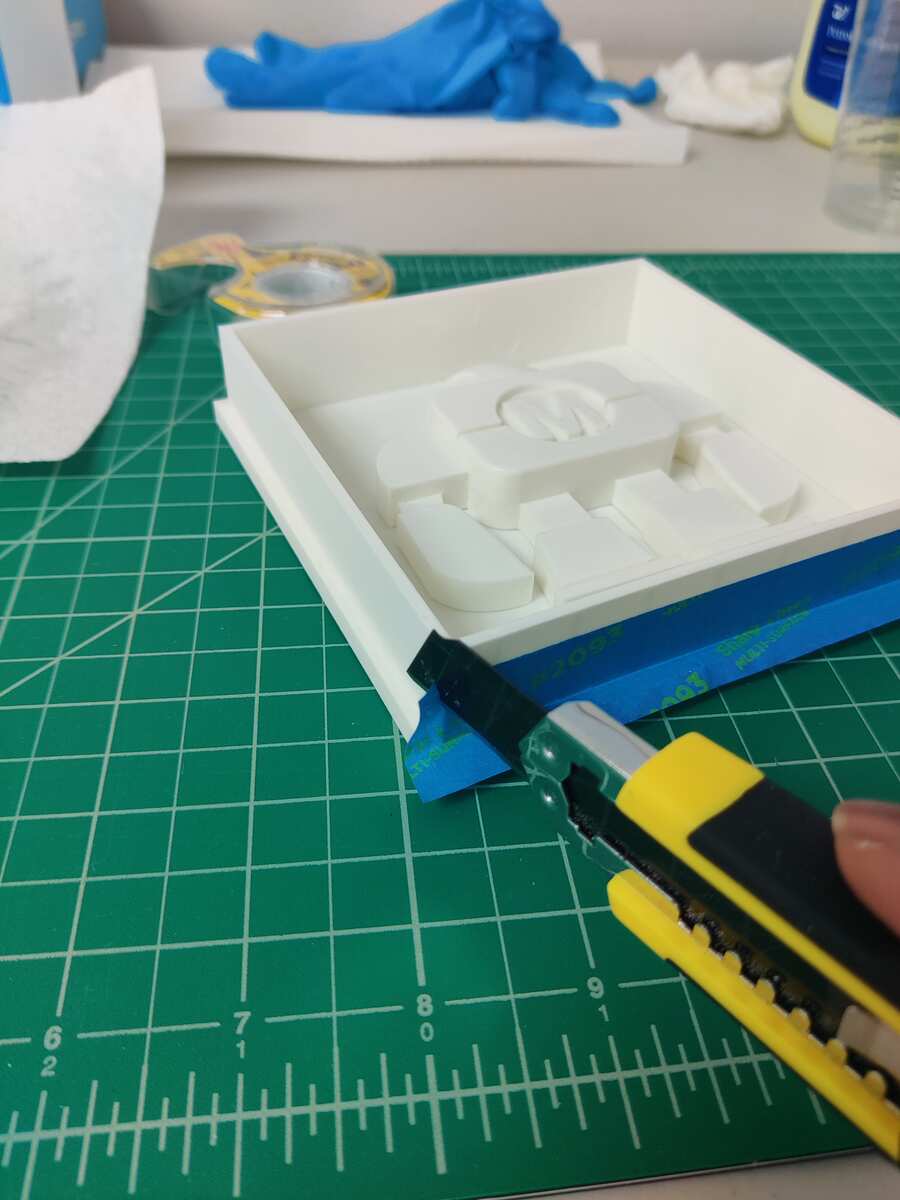 Utility knife trimming blue painter's tape sealing the mold box base