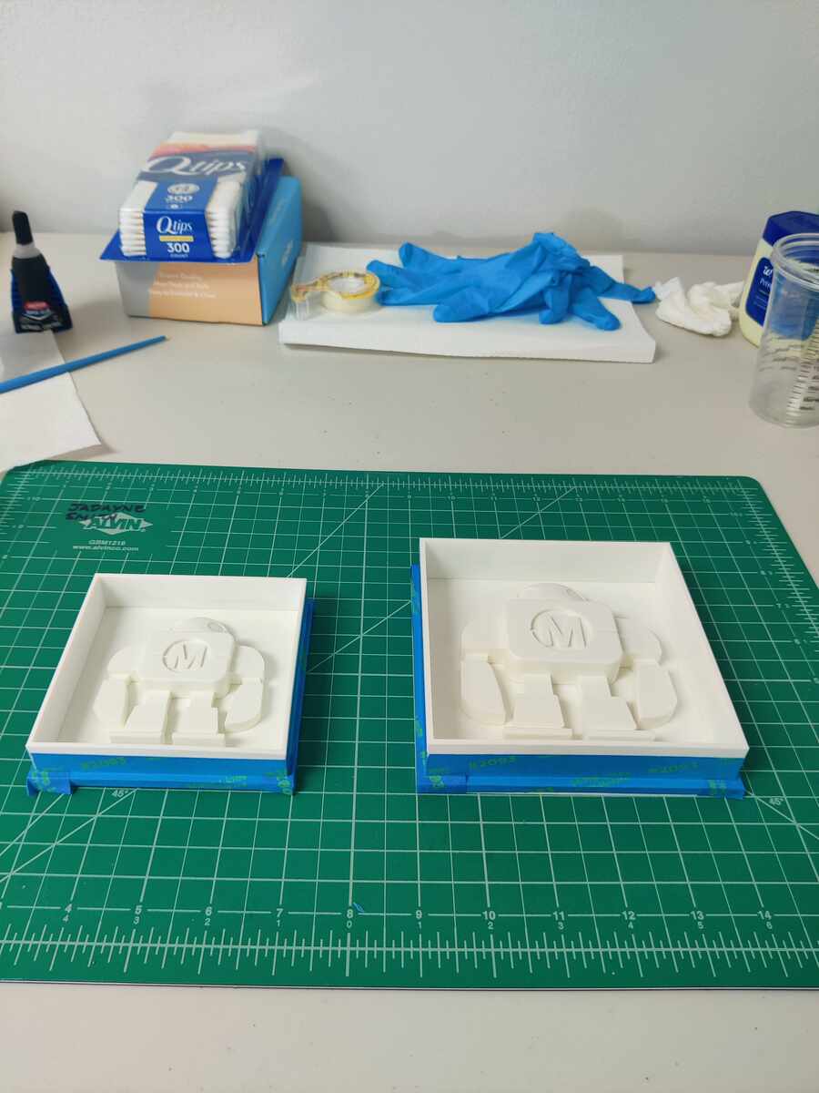Two sealed mold boxes with robot positives, positioned on cutting mat