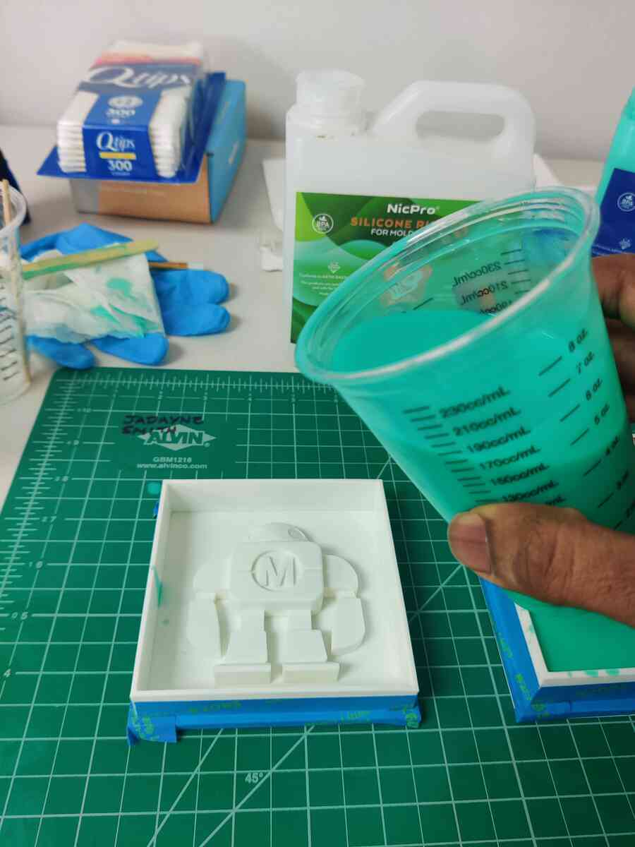 Pouring teal silicone from the mixing cup into the robot mold box