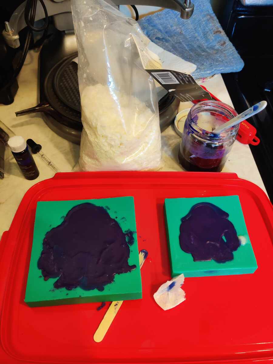 Purple-dyed soap poured over silicone molds on a red tray
