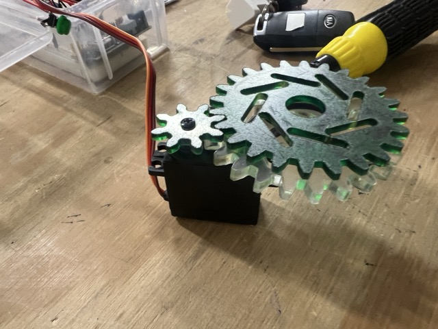 Three acrylic gears mounted on the servo motor — the transparent large gear and the green small gear are the final versions used