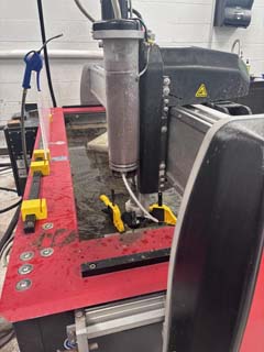 The stock material clamped to the waterjet table