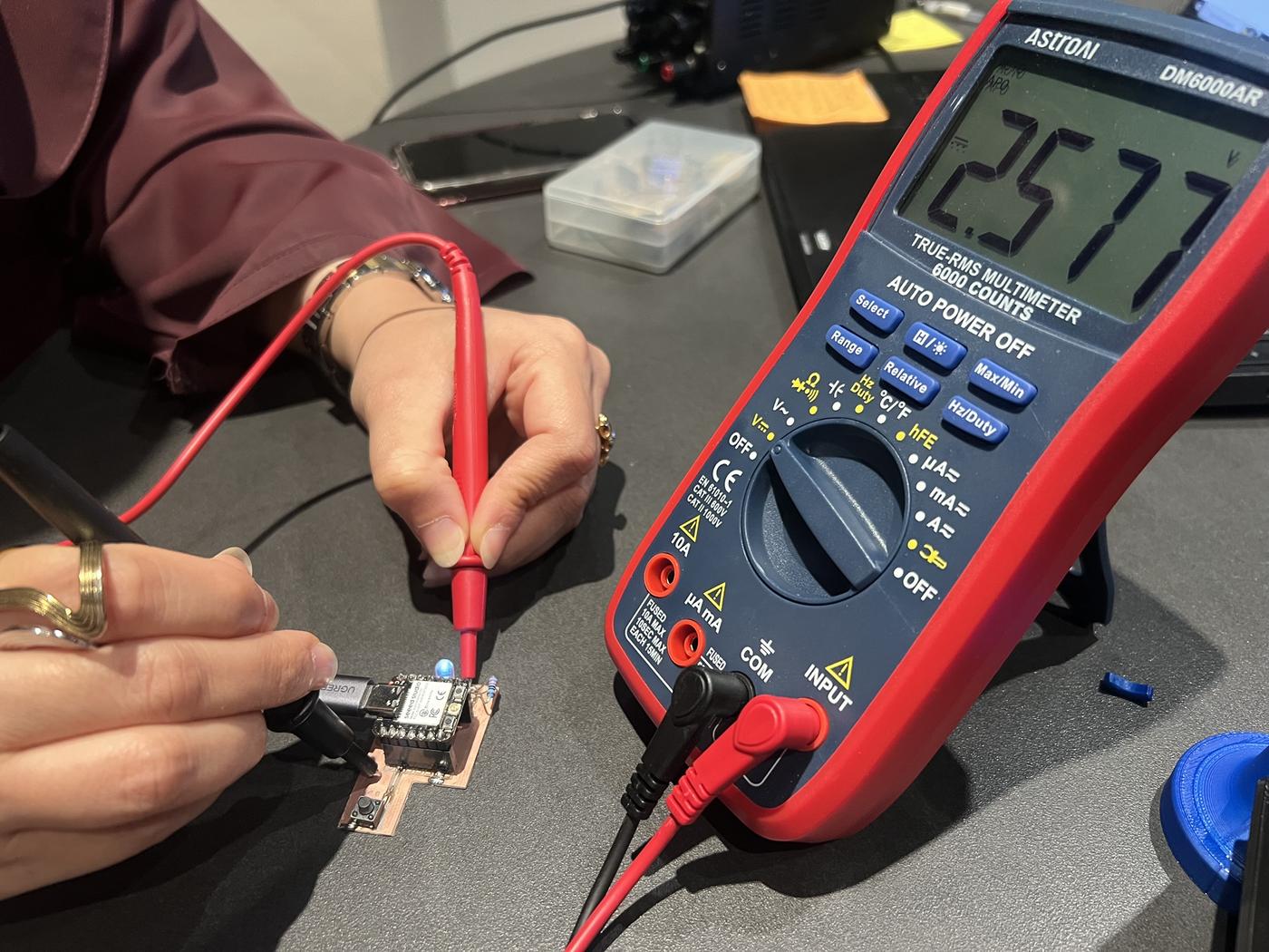 Multimeter probing the assembled PCB, reading 2.577 V DC