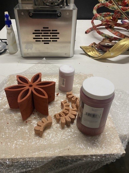 Bisque-fired clay flower drying alongside glaze containers in the workshop