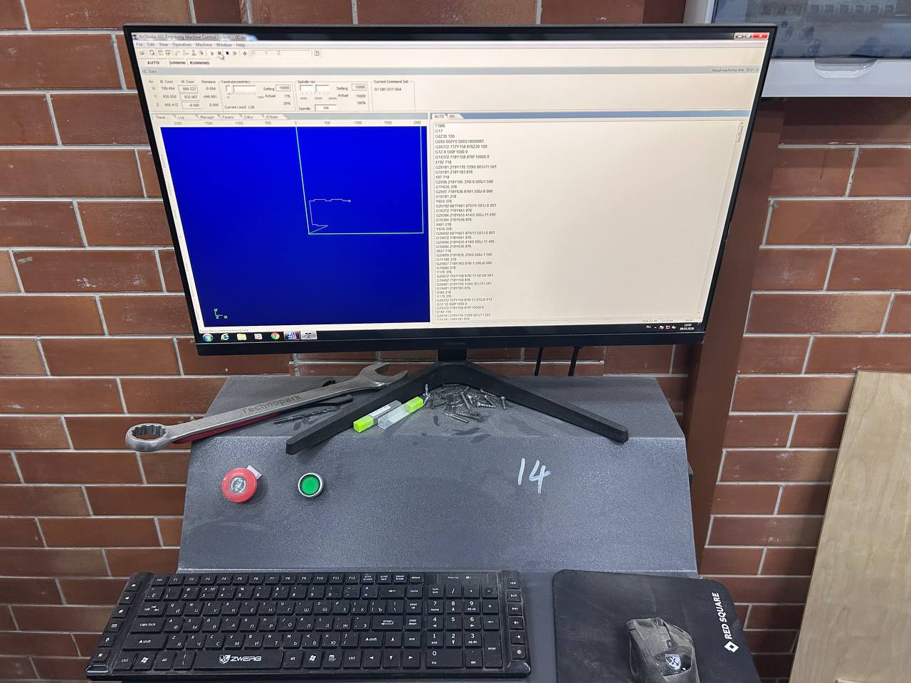 TechnoAllo CNC controller software on monitor — showing toolpath preview on blue canvas and G-code text on right side, red STOP button and green START button on machine console below keyboard