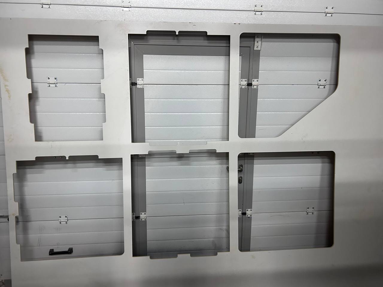 Six milled MDF panels laid out on the machine or against a surface — showing all the slot cutouts, hinge hardware already installed on some panels, clean cut edges visible